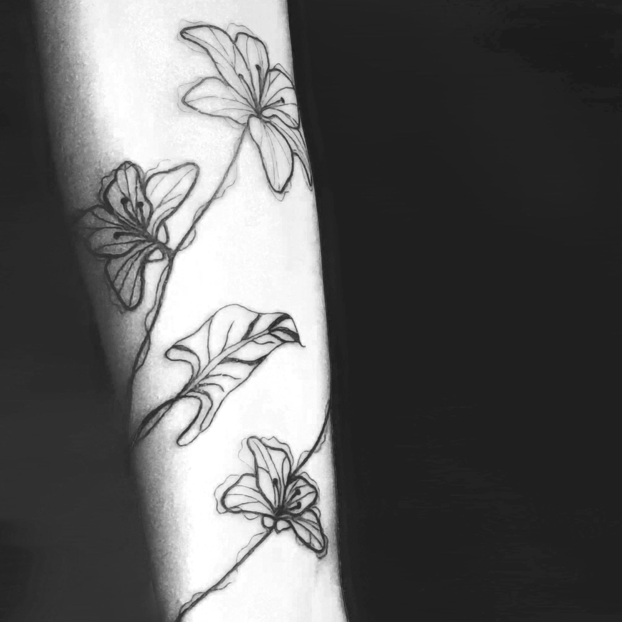 Tatuaje de flores y hojas con estilo fine line en el brazo